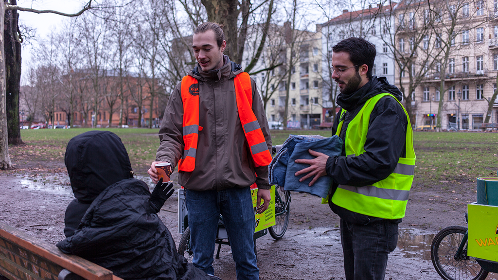 Studenten mit Lastenrädern geben einem Obdachlosen im Park einen Kaffee