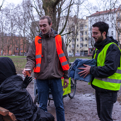 Studenten mit Lastenrädern geben einem Obdachlosen im Park einen Kaffee