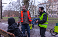 Studenten mit Lastenrädern geben einem Obdachlosen im Park einen Kaffee
